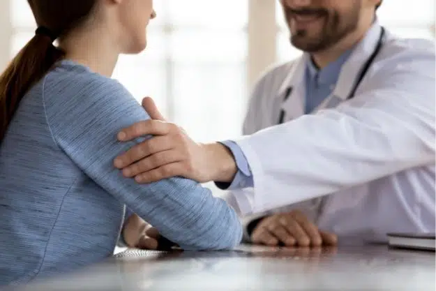 male doctor facing woman with his hand resting on her bicep in a comforting manner.