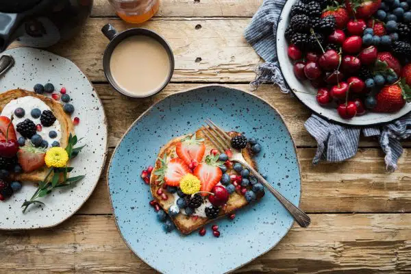 bowl of berries, blue plate of toast with fruit, cup of coffee on wooden table.