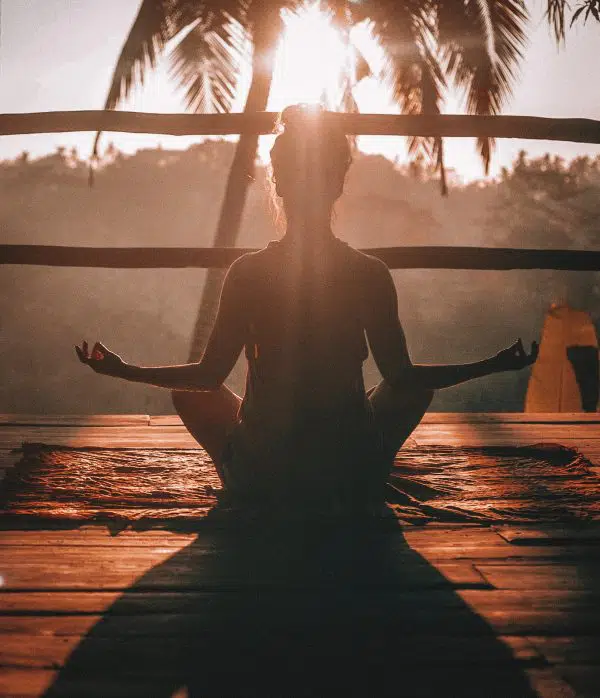 silhouette of woman meditating during sunrise with palm trees in background