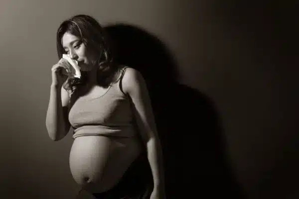pregnant woman crying, holding tissue to eyes.