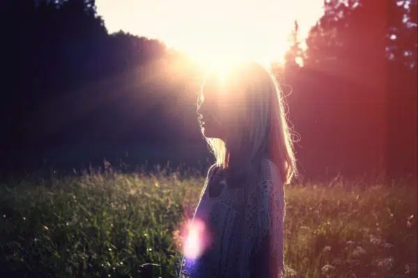 silhouette of woman standing in a field with sun glowing behind her.