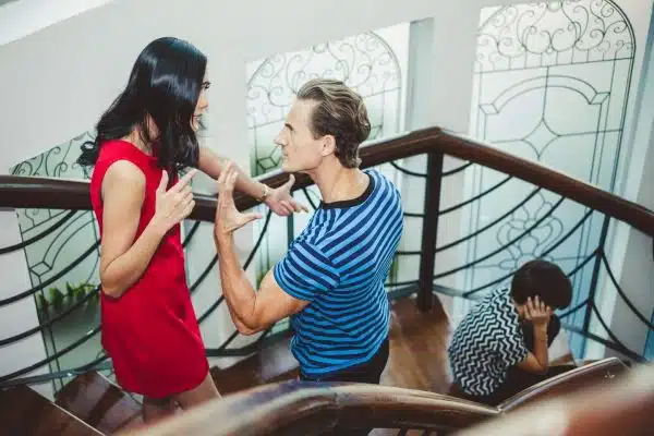parents arguing on staircase while child sits behind them covering ears