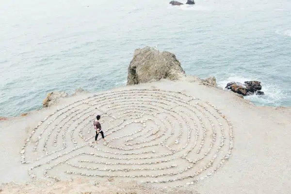 person walking into sand formation on edge of ocean cliff.