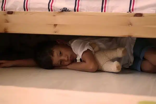small boy hiding under bed cuddling a stuffed animal