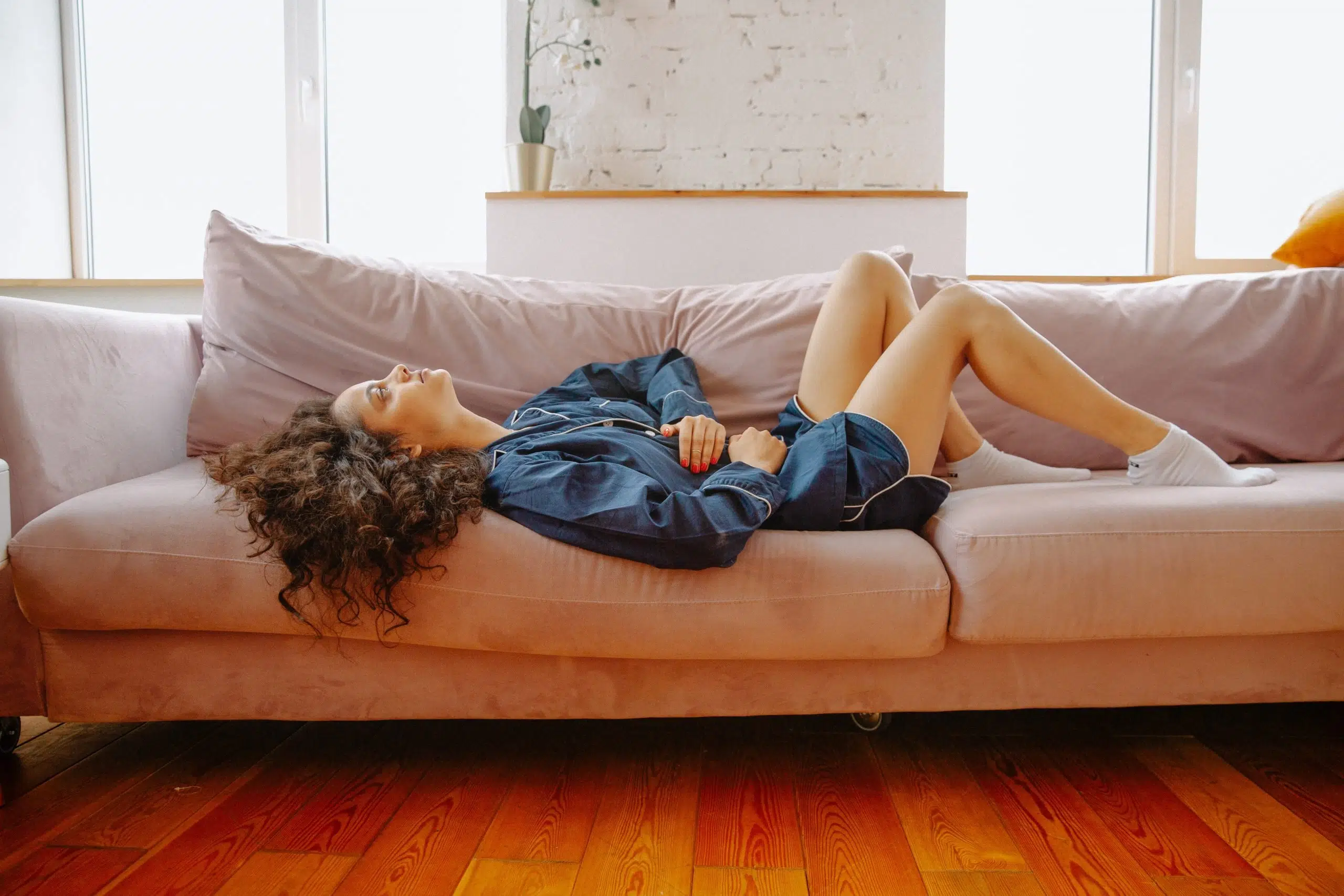 woman laying on couch. holding stomach in pain