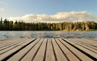 planks of dock looking out onto a lake with pine trees lining opposite end of lake.