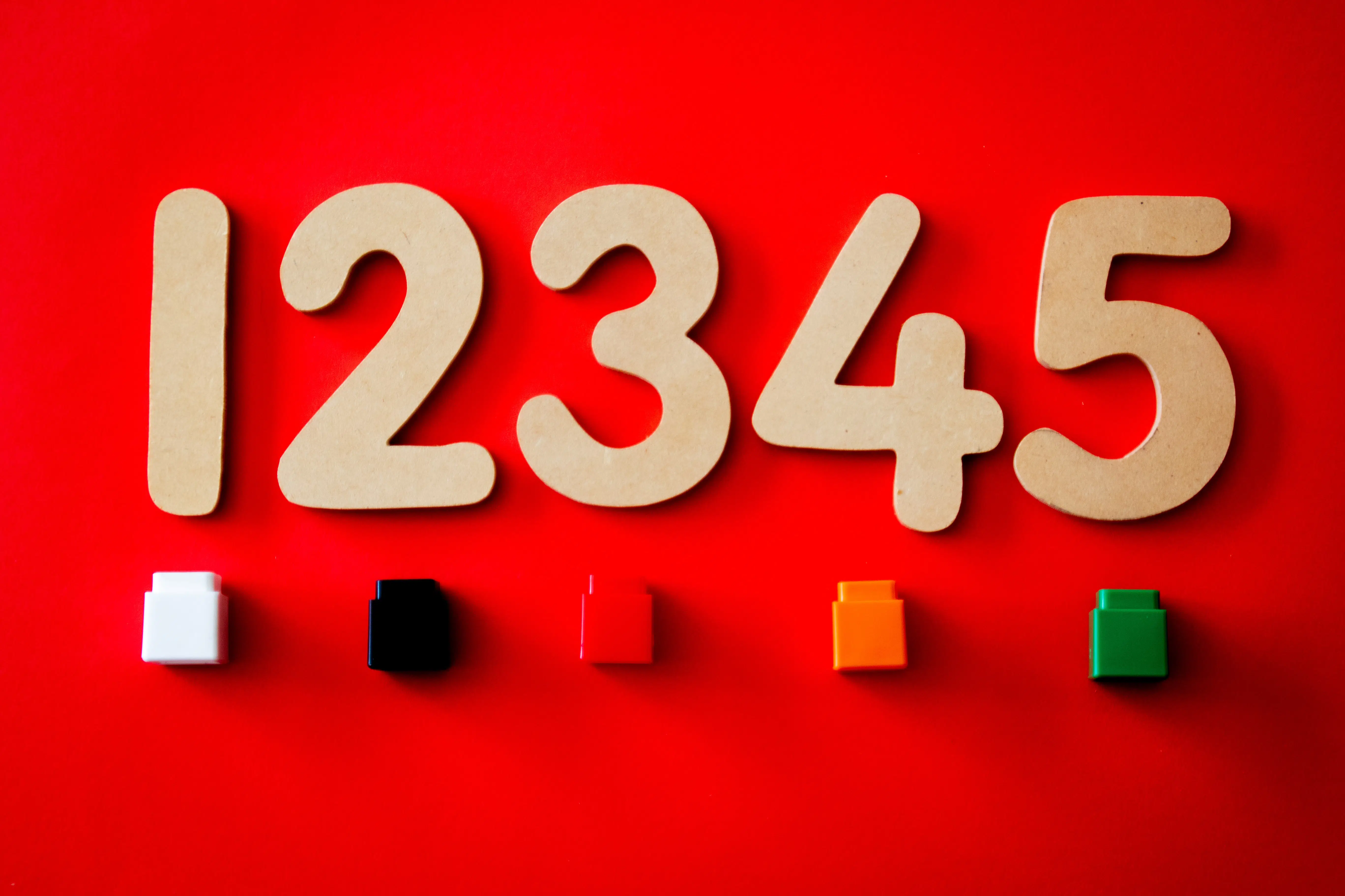 red background with cardboard cutout numbers one through five lined up and a different colored lego block under each number.