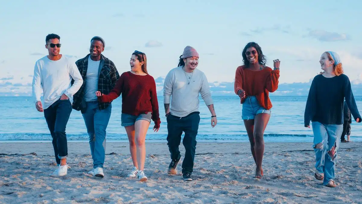 Six young adults walking on the beach talking and laughing.