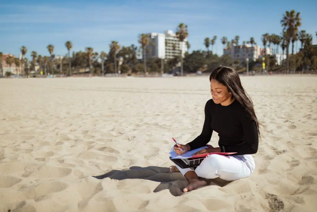 woman sitting on beach writing in a journal.