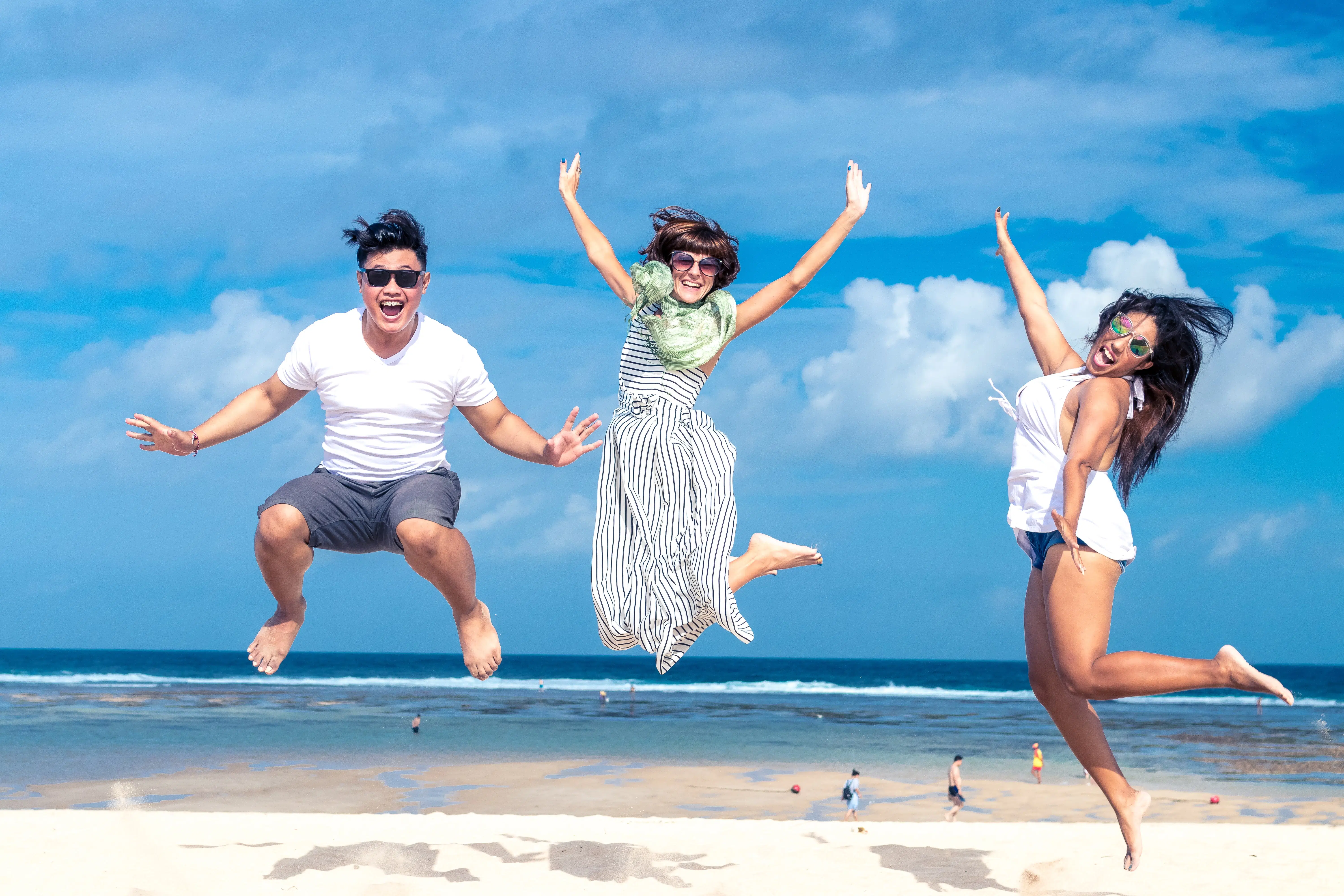 three people on a beach jumping in the air for joy.
