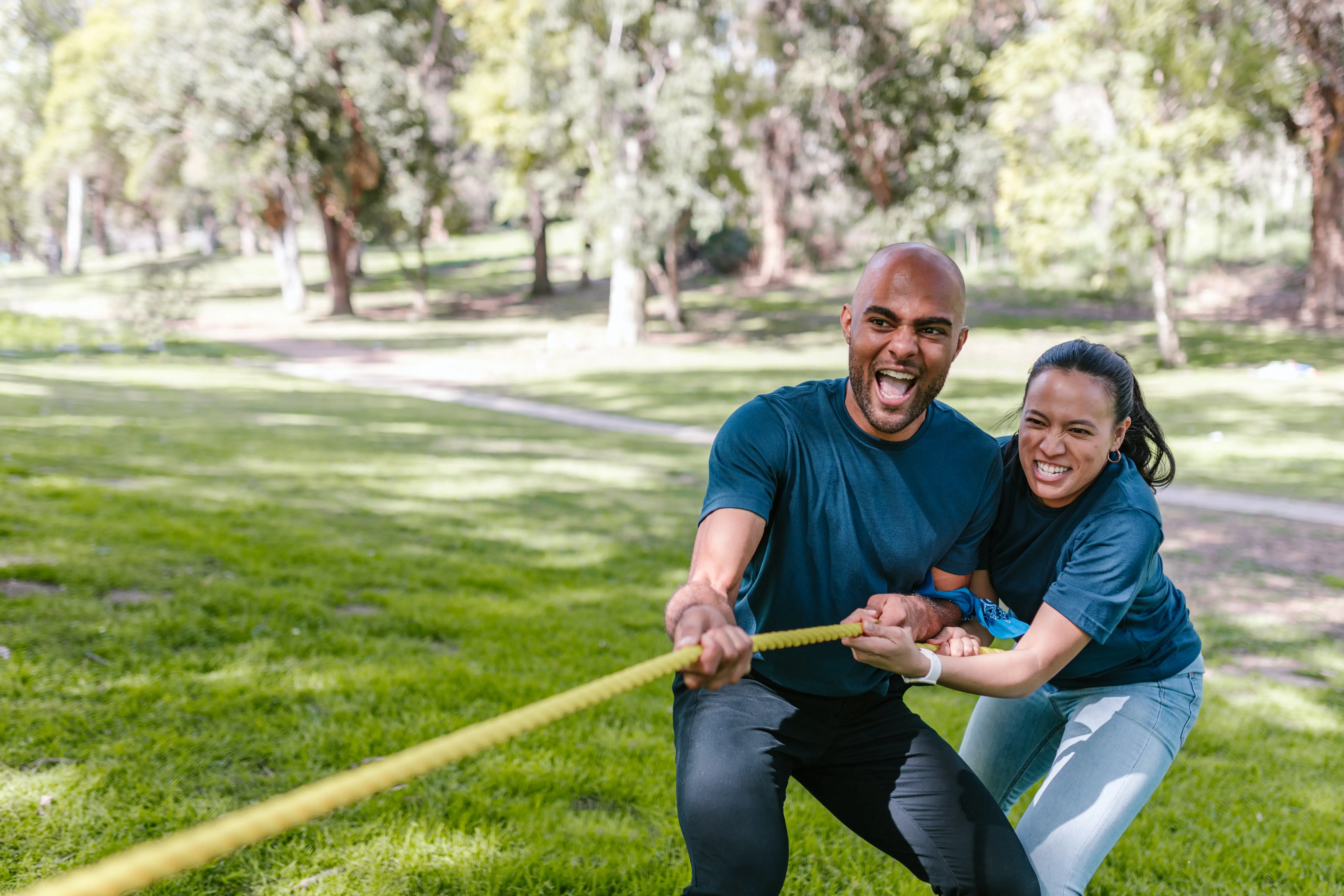 two people in a park, pulling a rope during tug-of-war game.