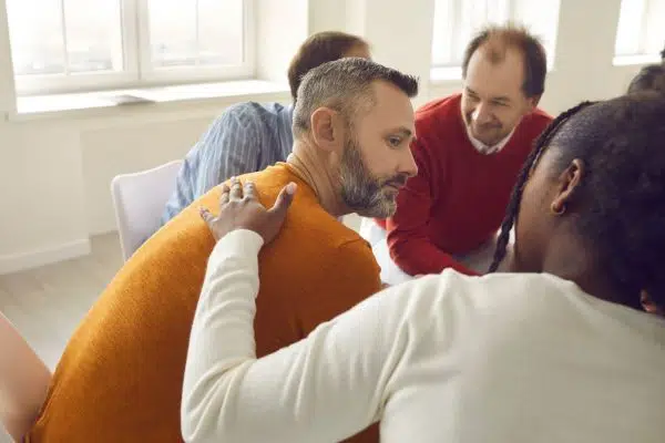 circle of people talking, man being comforted by someone next to him.