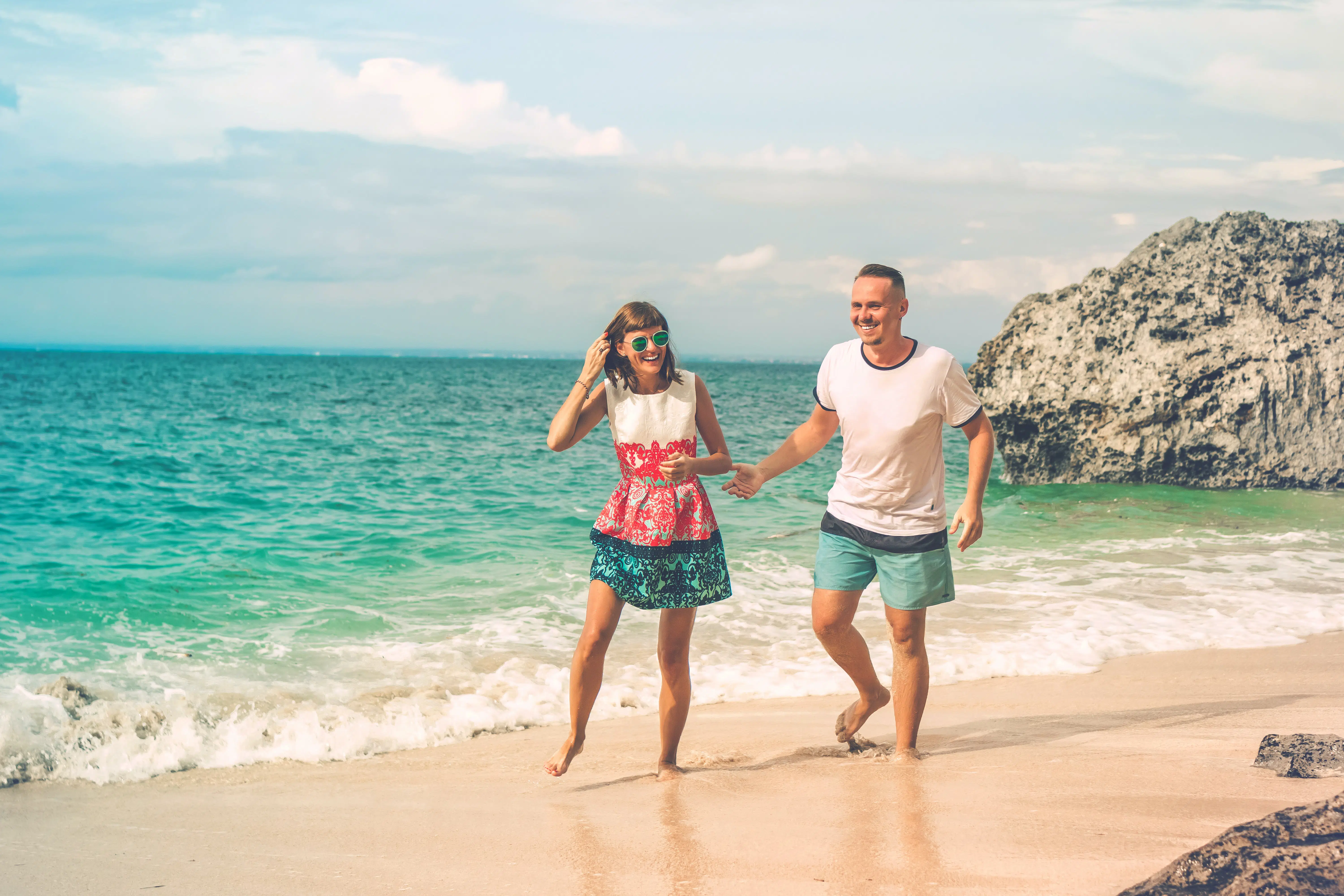 couple holding hands walking along beach.