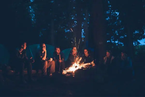 group of people sitting around a campfire, camping in the woods.