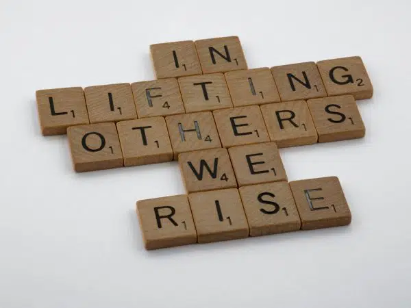 scrabble tiles reading "in lifting others we rise."