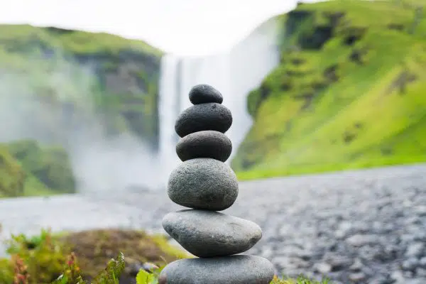 stack of black river rocks with waterfall scene in background.