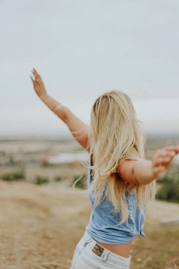 back view of a woman standing on a hill with arms outstretched.