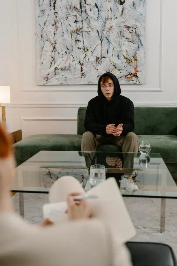 young man looking disheveled sitting on couch and speaking to a therapist across from him.