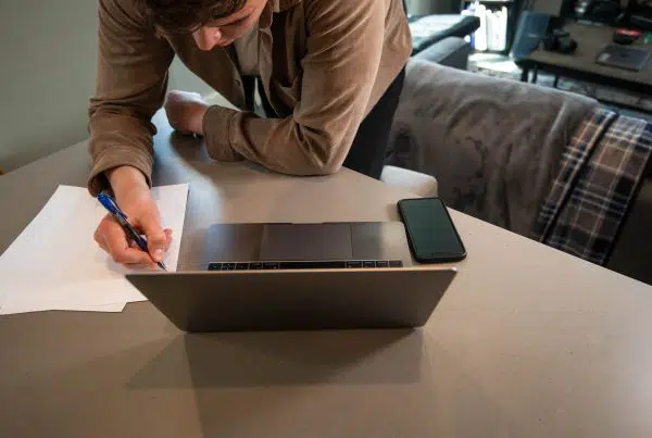 person looking at laptop and writing notes on a sheet of paper.