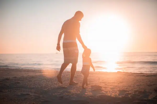 silohuette of man holding child's hand walking words ocean.