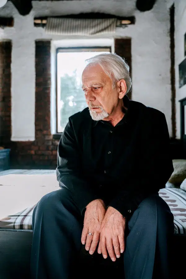 older man sitting on bed looking sad.