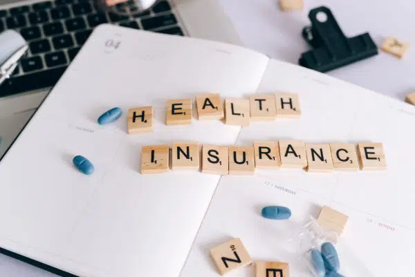 tiles spelling out health insurance, surrounded by pills.