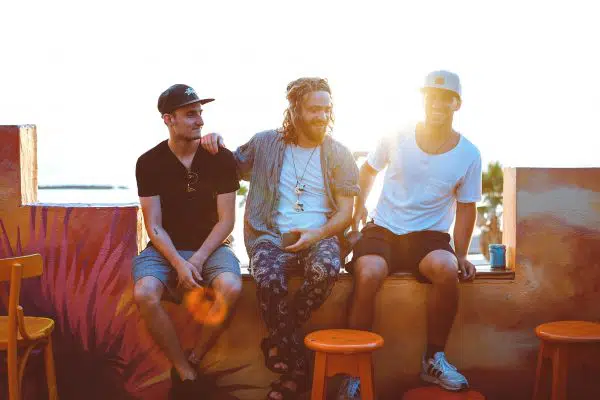 three guys sitting on low wall laughing with sun setting behind them.