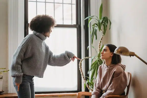woman standing and yelling at woman who is sitting.