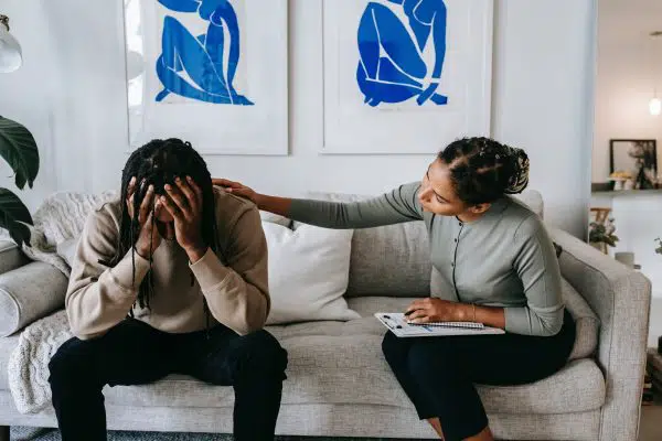 therapist with her hand on a mans shoulder as he buries his head in his hands.