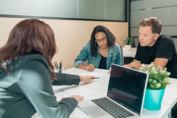 couple sitting at desk with a woman who is reviewing paperwork with them.