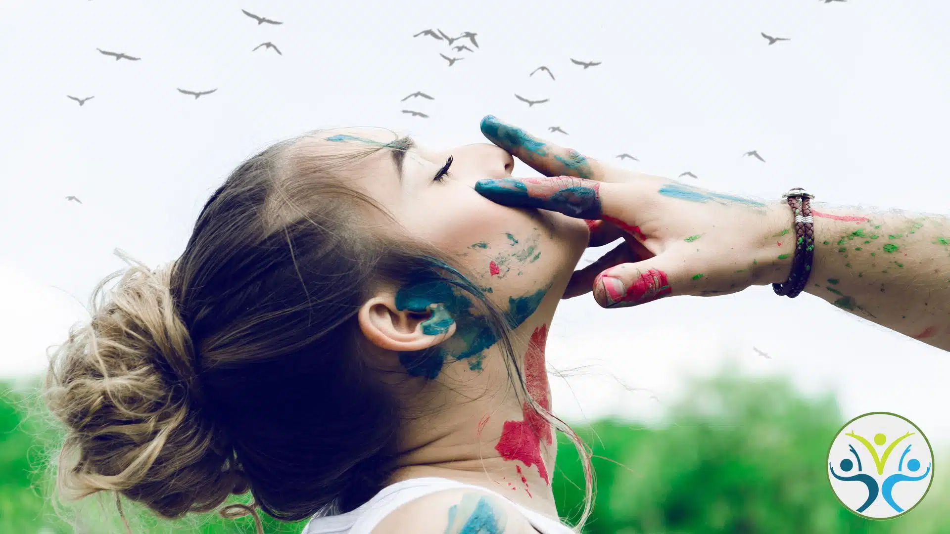 young woman with blue and red paint on her face and neck is tilting head back while someone else's painted hand is gently over her mouth.