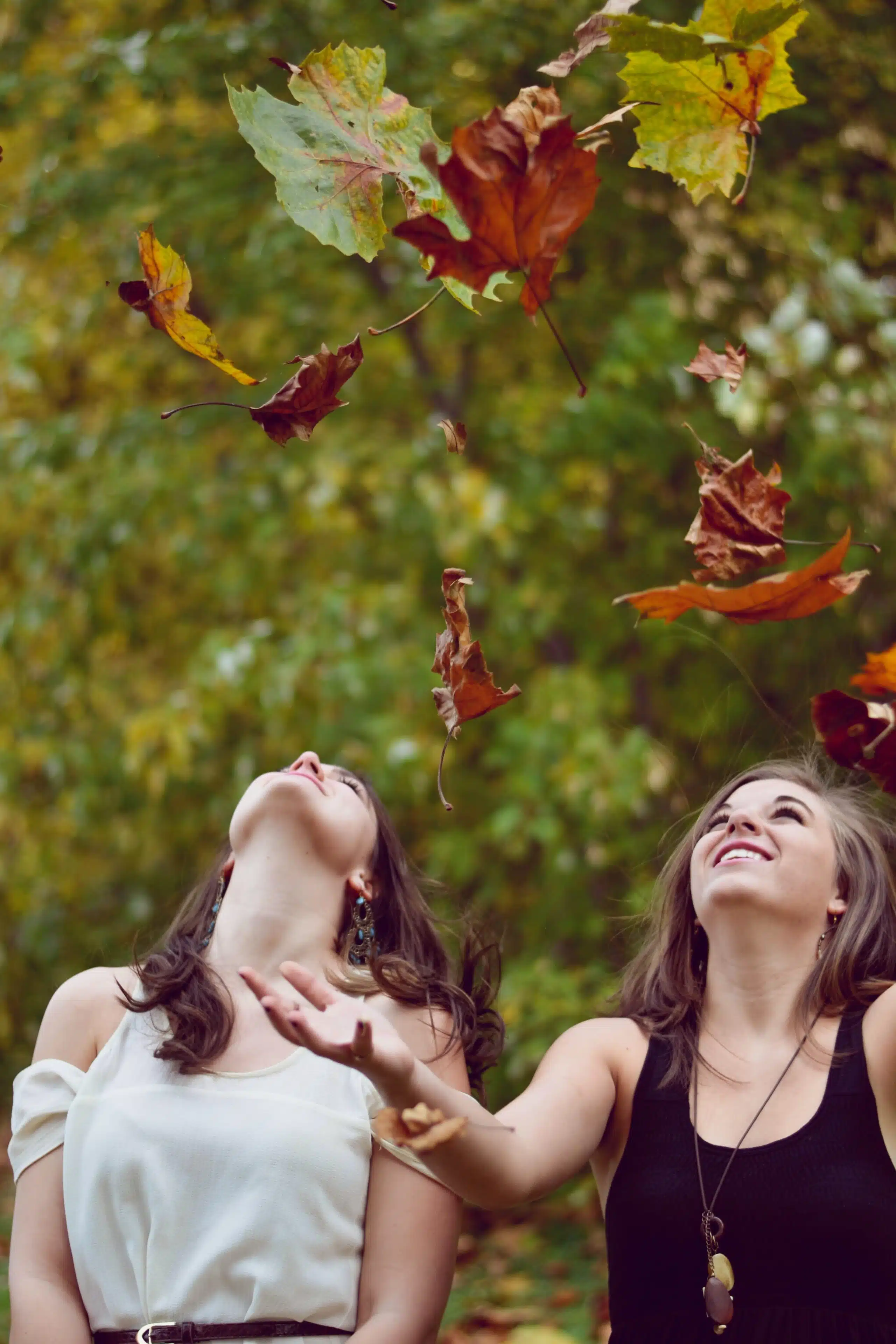 two women smiling happily as they throw fall leaves into the air.