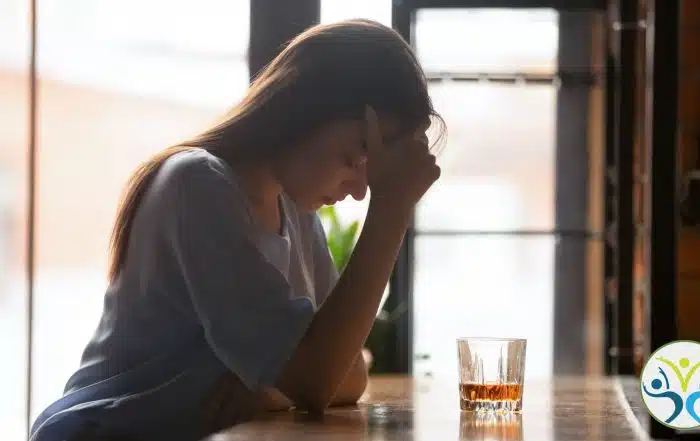 woman sitting at a bar with her head in her hand and a glass of whiskey in front of her.