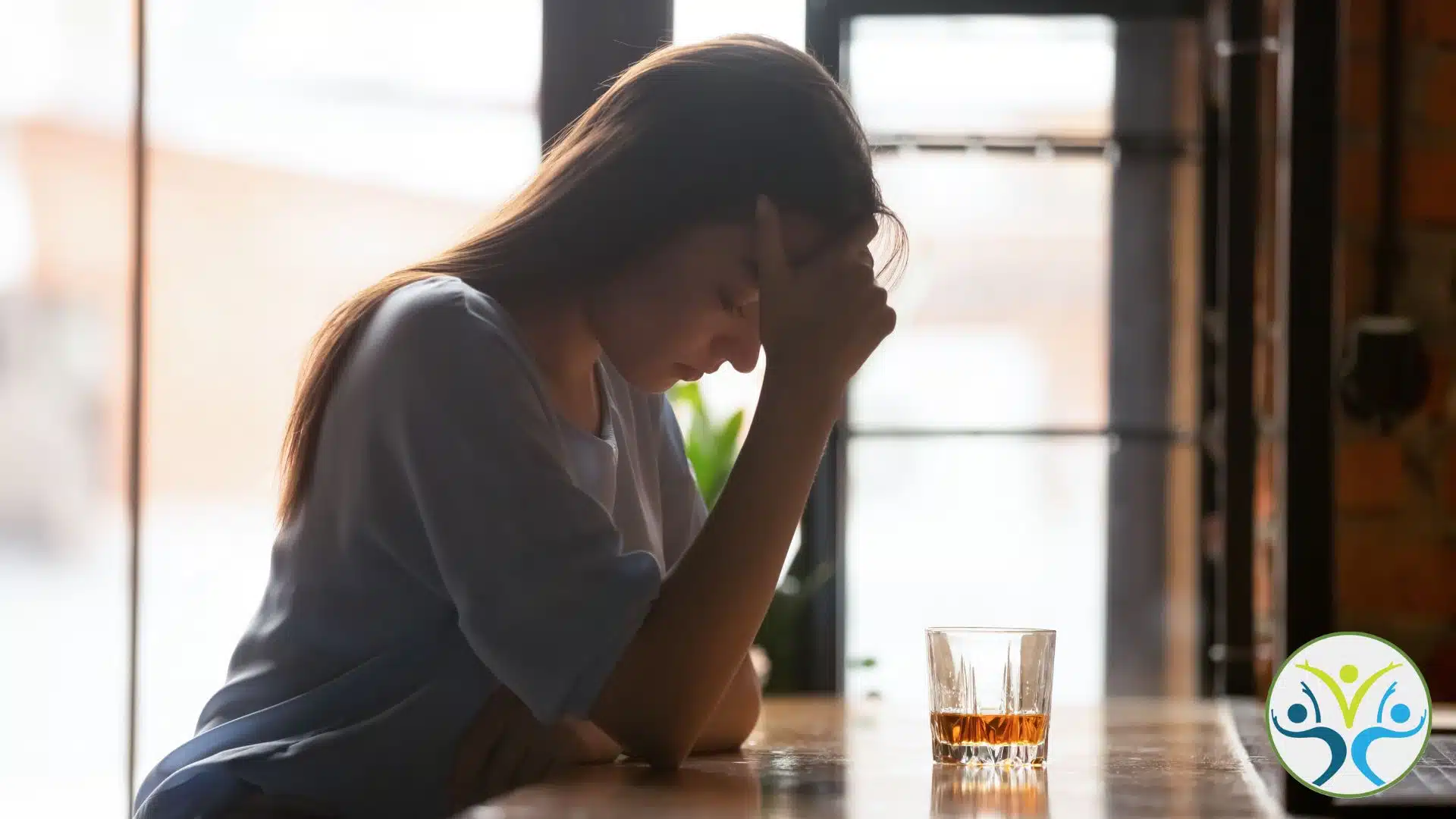 woman sitting at a bar with her head in her hand and a glass of whiskey in front of her.